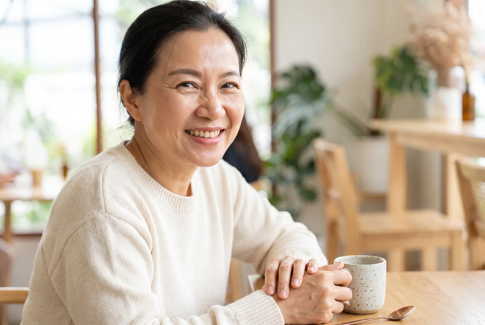 Smiling mature woman with natural expression seated beside a bright cafe window