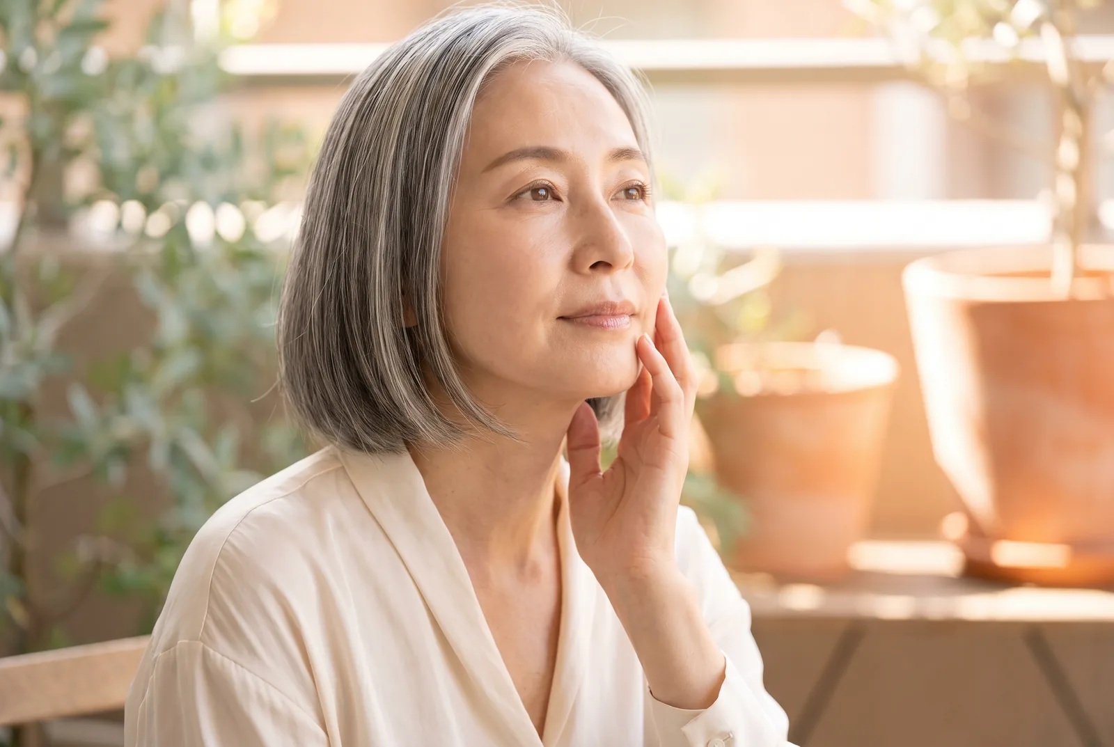 Japanese woman with radiant skin touching her cheek on a sunlit terrace